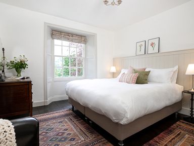 A bedroom with a bed with pillows two framed pictures a wooden dresser a window and two table lamps at Thorney How in Grasmere