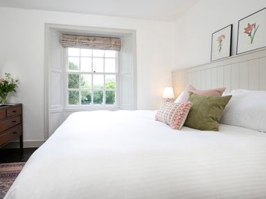A bedroom with a large bed with pillows a bedside lamp a wooden chest of drawers and a window at Thorney How in Grasmere