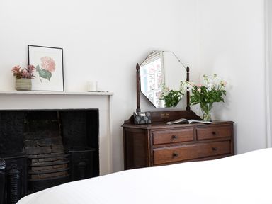 A wooden dresser with mirror and flowers next to a black fireplace in a bedroom at Thorney How in Grasmere
