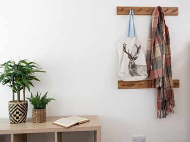 A wooden table with two potted plants and an open book next to wooden wall hooks holding a tote bag and a plaid scarf at Thorney How in Grasmere