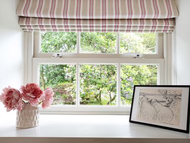 A window with a striped roman blind pink flowers in a vase and a framed sketch of sheep on the windowsill at Thorney How in Grasmere