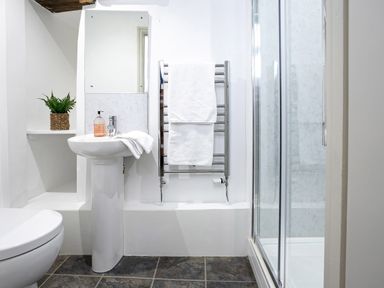 A bathroom with a sink and mirror a towel rack with white towels a toilet and a shower enclosure at Thorney How in Grasmere