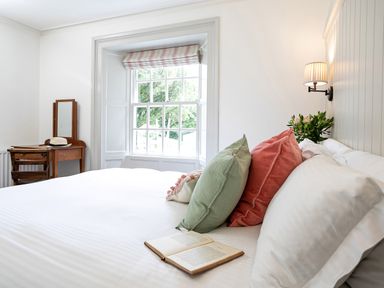 A bedroom with a bed with pillows and an open book near a window and a wooden dressing table with a mirror at Thorney How in Grasmere