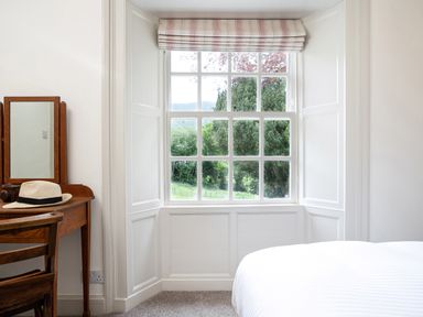 A bedroom corner with a window showing outdoor trees a wooden desk with a mirror and hat at Thorney How in Grasmere