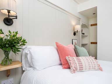 A bedroom with a white bed, decorative pillows, wall lamps, a vase with flowers, and a small shelf at Thorney How in Grasmere