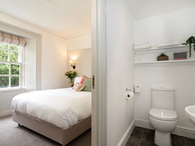 A bedroom with a bed and window next to a bathroom with a toilet and shelves at Thorney How in Grasmere