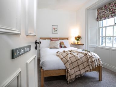 A bedroom with a wooden bed with pillows and a plaid blanket near a window with floral curtains at Thorney How in Grasmere