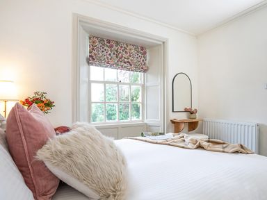 A bedroom with a bed with pillows and a blanket near a window with floral blinds and a small wall-mounted shelf with a mirror at Thorney How in Grasmere