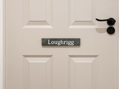 A beige panel door with a black nameplate that says Loughrigg and a black door handle