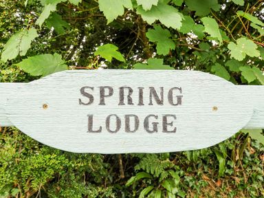 A wooden sign with the text Spring Lodge surrounded by green leaves and foliage at Eastcott near Kilkhampton
