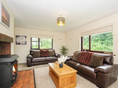 A living room with two brown leather sofas a wooden coffee table a fireplace and large windows at Spring Lodge in Eastcott near Kilkhampton