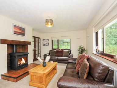A living room with two brown leather sofas a wooden coffee table a fireplace and windows showing greenery at Spring Lodge in Eastcott near Kilkhampton