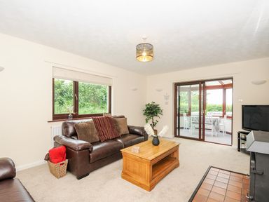A living room with brown leather sofas a wooden coffee table a television and a sliding door to a dining area at Spring Lodge in Eastcott near Kilkhampton