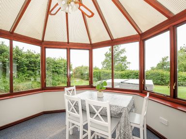 A dining area with a table and four chairs in a glass conservatory at Spring Lodge in Eastcott near Kilkhampton
