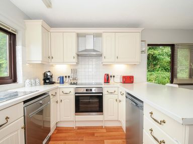 A kitchen with cream cabinets stainless steel appliances and a window showing greenery at Spring Lodge in Eastcott near Kilkhampton