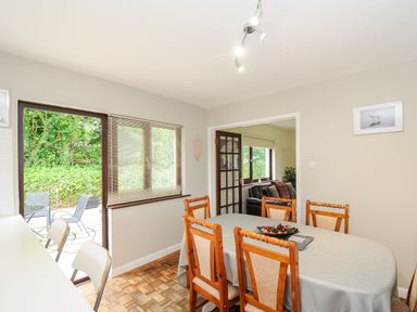 A dining area with a table covered by a cloth surrounded by wooden chairs next to a window and a glass door leading outside at Spring Lodge in Eastcott near Kilkhampton