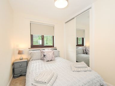 A bedroom with a double bed bedside table lamp window and mirrored wardrobe at Spring Lodge in Eastcott near Kilkhampton
