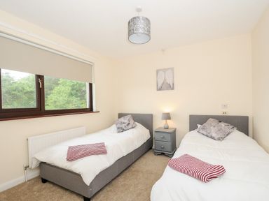 A bedroom with two single beds a window and a nightstand with a lamp at Spring Lodge Eastcott near Kilkhampton