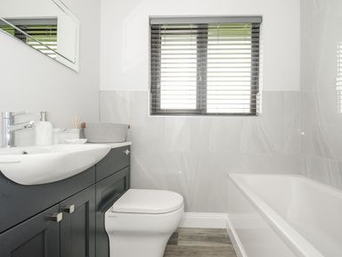 A bathroom with a bathtub a toilet a sink with countertop a window with blinds and a wall mirror at Spring Lodge in Eastcott near Kilkhampton