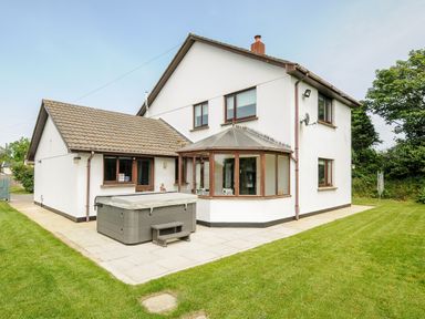 A two story house with a tiled roof patio with a hot tub and surrounding lawn at Spring Lodge in Eastcott near Kilkhampton