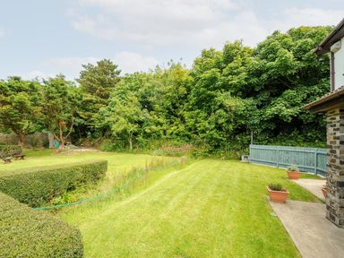 A garden with neatly cut grass hedges and potted plants near a house with a brick wall and wooden fence at Spring Lodge Eastcott near Kilkhampton