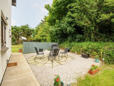 An outdoor patio area with a round table and four chairs surrounded by gravel and plants at Spring Lodge in Eastcott near Kilkhampton