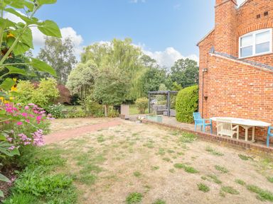 A garden with a path, flowers, trees, patio furniture, and a brick house at Willow Cottage in Hickling near Catfield