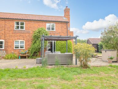 A backyard with a brick house patio outdoor seating under a pergola and garden shed at Willow Cottage in Hickling near Catfield