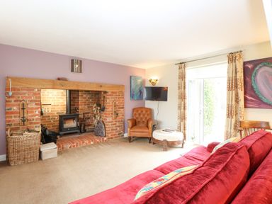 A living room with a brick fireplace a red sofa an armchair a wall-mounted television and curtains at Willow Cottage in Hickling near Catfield