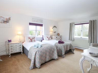 A bedroom with two single beds side by side white furniture and windows with curtains at Willow Cottage in Hickling near Catfield