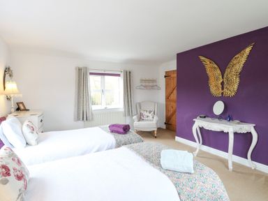 A bedroom with two single beds a white dressing table and a cream armchair at Willow Cottage in Hickling near Catfield