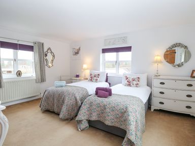 A bedroom with two single beds floral bedding floral cushions two windows and a white dresser at Willow Cottage in Hickling near Catfield