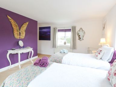 A bedroom with two beds white furniture purple wall and decorative gold wings at Willow Cottage in Hickling near Catfield