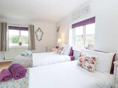 A bedroom with two single beds with white bedding and floral pillows at Willow Cottage in Hickling near Catfield