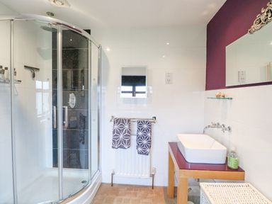 A bathroom with a glass shower enclosure towels on a radiator a sink on a wooden countertop and a mirror at Willow Cottage in Hickling near Catfield