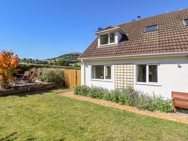 A garden with a lawn wooden chairs and a white house with windows at Cam O'r Fechan Annexe in Llangollen