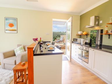 A kitchen with white cabinets a black countertop and an open door leading outside at Cam O'r Fechan Annexe in Llangollen