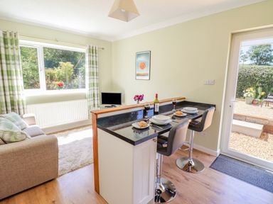 A kitchen bar with two stools set for a meal next to a living area with a sofa and window at Cam O'r Fechan Annexe in Llangollen