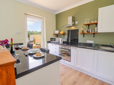 A kitchen with white cabinets black countertops a stove microwave kettle and breakfast set on a counter at Cam O'r Fechan Annexe Llangollen