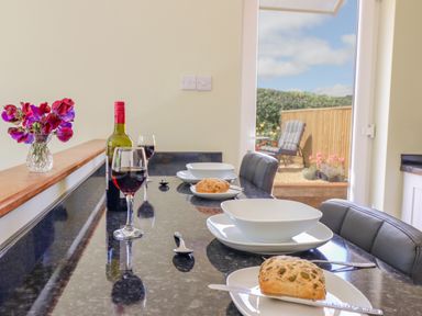 A kitchen counter set with bowls plates bread and glasses of red wine with a door open to a garden at Cam O'r Fechan Annexe in Llangollen