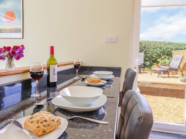 A kitchen counter set with plates bowls bread wine glasses and a bottle with a view of an outdoor sitting area at Cam O'r Fechan Annexe in Llangollen