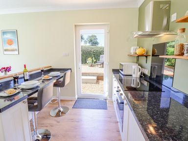 A kitchen with bar stools plates wine and bread on a counter and a glass door leading outside at Cam O'r Fechan Annexe in Llangollen