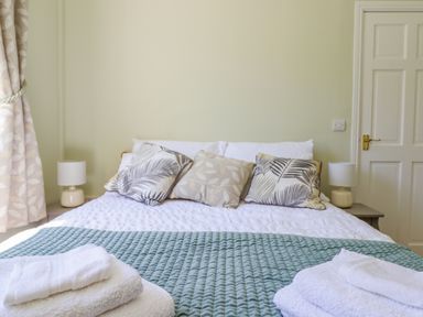 A bedroom with a bed with patterned pillows bedside tables with lamps towels on the bed and a door in the background at Cam O'r Fechan Annexe in Llangollen