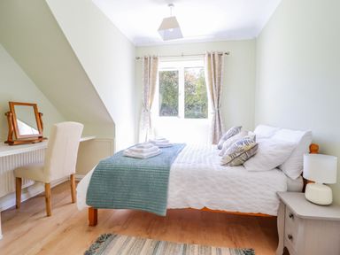 A bedroom with a double bed, pillows, folded towels, side table with lamp, chair, mirror, and window with curtains at Cam O'r Fechan Annexe in Llangollen