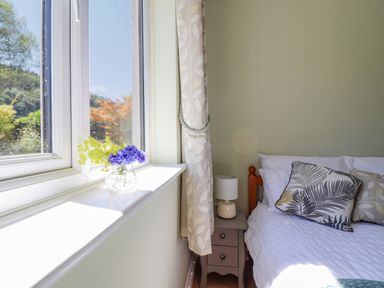 A bedroom with a window showing flowers on the windowsill and a bed with patterned pillows at Cam O'r Fechan Annexe in Llangollen