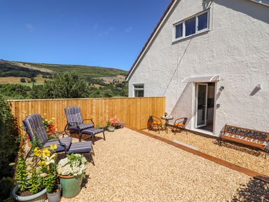 An outdoor patio area with striped chairs potted plants a small table with two chairs and a bench next to a white house at Cam O'r Fechan Annexe in Llangollen