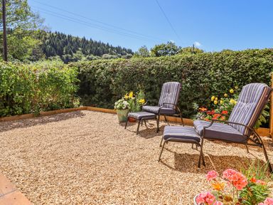 A gravel patio with two striped armchairs and footrests surrounded by potted flowers and a hedge at Cam O'r Fechan Annexe in Llangollen