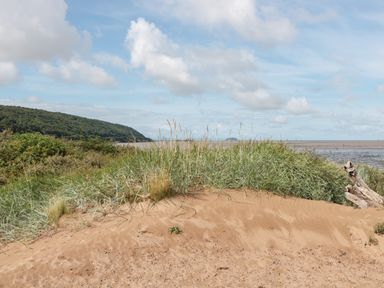 A sandy beach with tall grass and a hill in the background at Bluebell Lodge Meadow view lodges in Brean