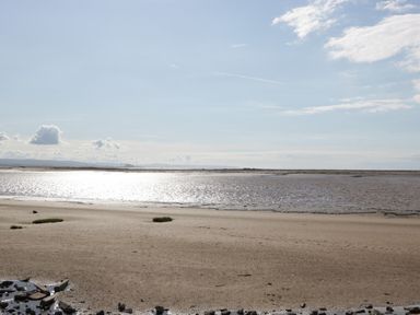 A sandy beach with water and rocks under a blue sky