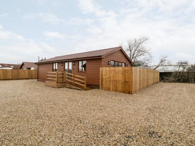A single story lodge with wooden exterior and a ramp surrounded by gravel and wooden fencing at Bluebell Lodge Meadow view lodges in Brean